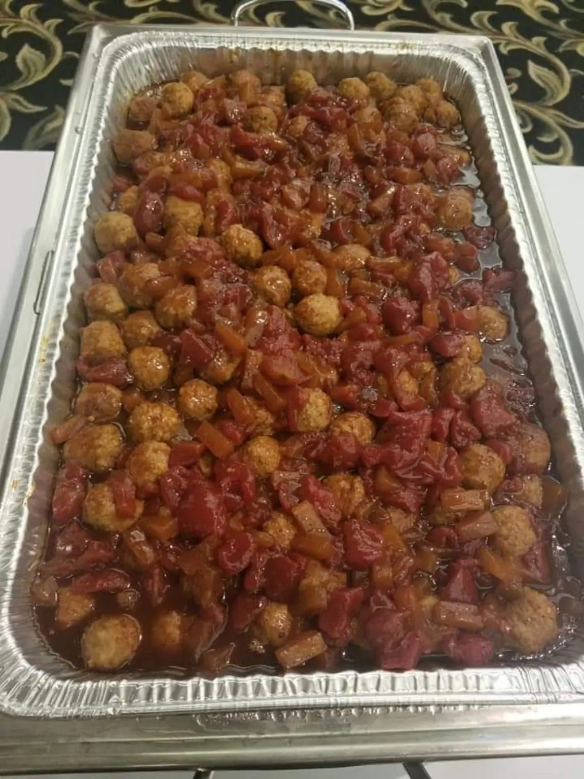 A full catering tray of glazed meatballs and sliced sausage